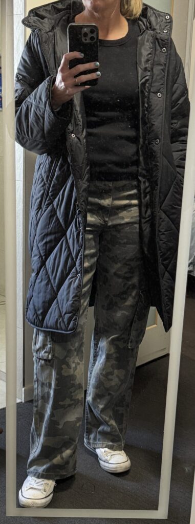 Outfit consisting of black puffer, black shirt, camo pants, white shoes.