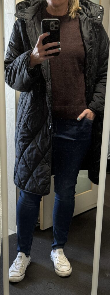 Outfit consisting of blue jeans, brown sweater, black puffer, white shoes.