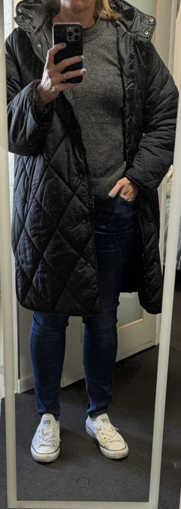 Outfit consisting of black puffer, charcoal sweater, jeans, white shoes.